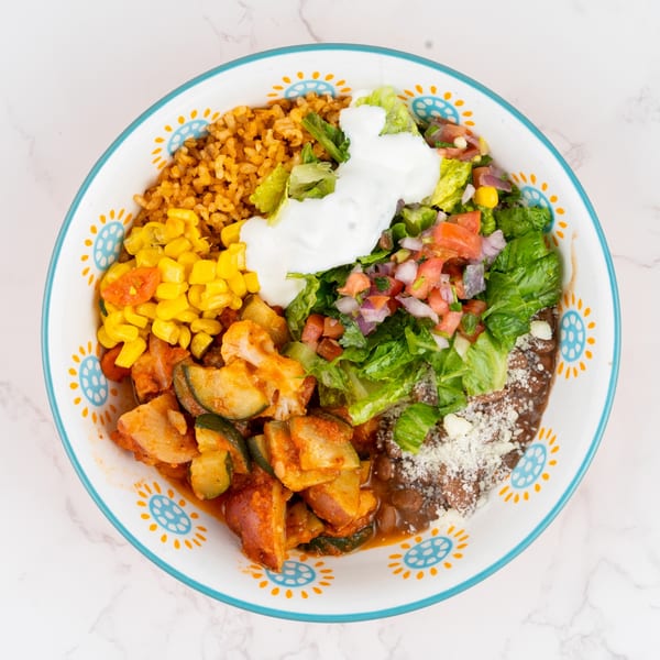 Colorful bowl with rice, corn, zucchini, beans, lettuce, pico de gallo, and sour cream.