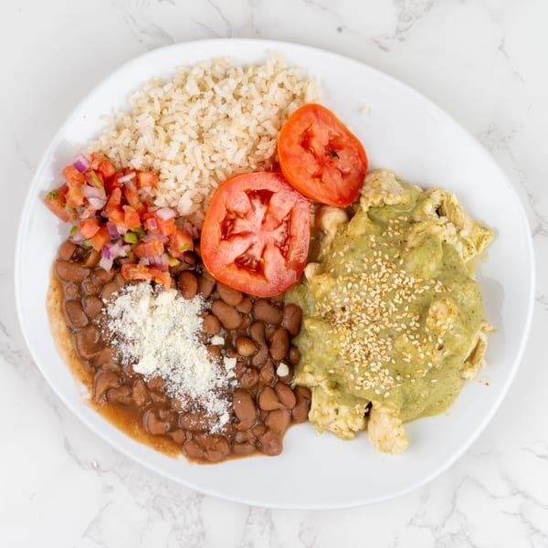 A white plate with chicken in green sauce, rice, beans, pico de gallo, and tomato slices.
