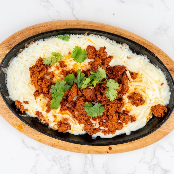 Melted white cheese with chorizo and cilantro in a black skillet on a wooden board.