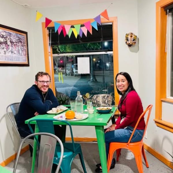 A smiling couple enjoys a meal at a green table in Tenoch Mexican Grill, decorated with colorful banners.