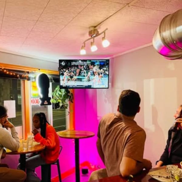 Diners at Tenoch Mexican Grill watch a basketball game on a TV in a pink-lit dining area.