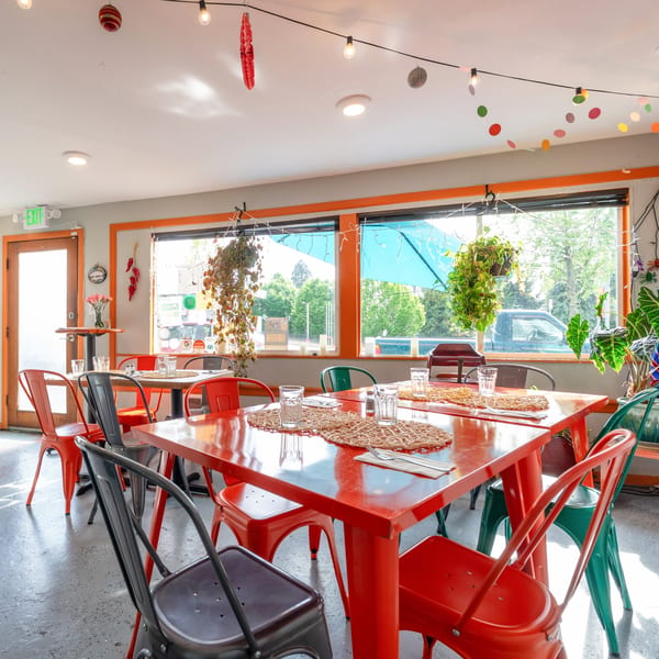 A vibrant restaurant interior with red tables and colorful chairs, bathed in natural light from large windows.