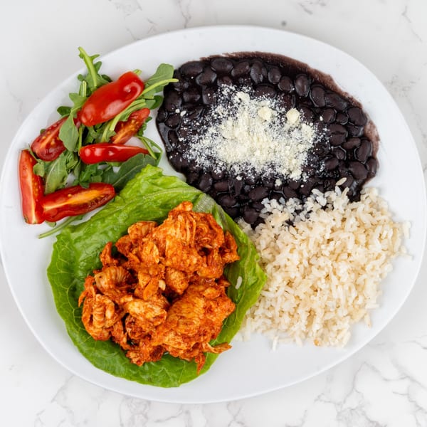 A white plate with black beans, rice, chicken in a lettuce cup, and a side salad.