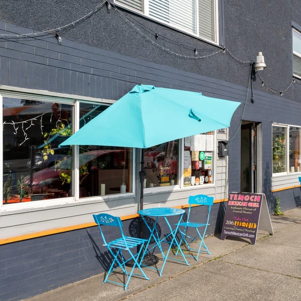 Tenoch Mexican Grill's outdoor seating with a turquoise umbrella, table, and chairs on a sunny day.