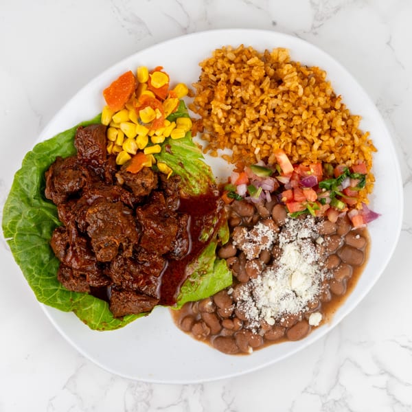 Braised beef on lettuce with rice, beans, corn, and pico de gallo on a white plate.